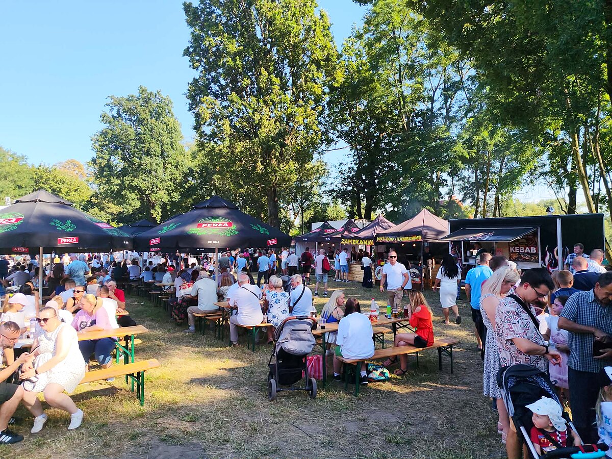 Stoiska gastronomiczne, food trucki i ławostoły pod parasolami na festynie w słoneczny dzień